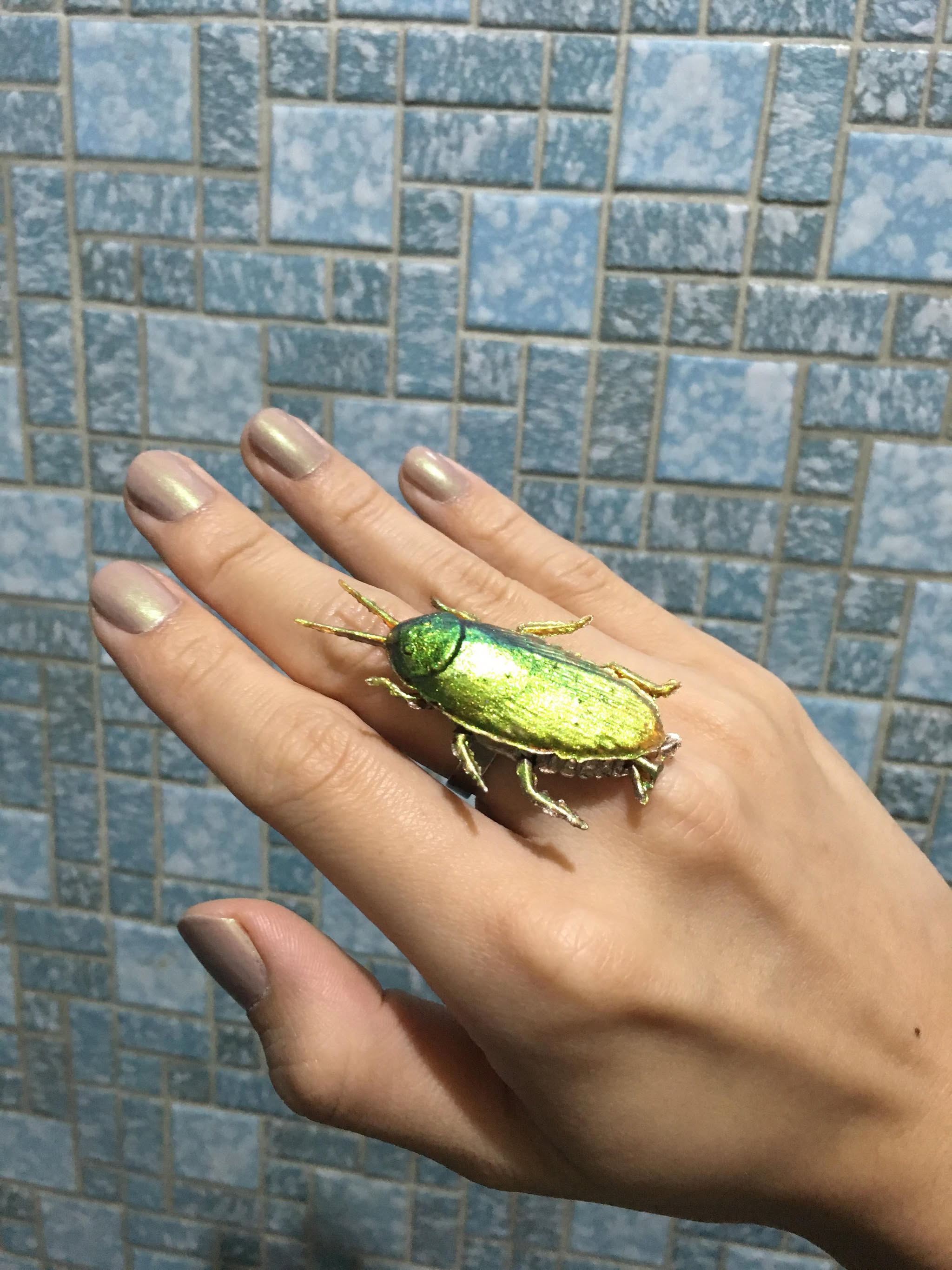 Close view of the Titanopsis cockroach ring worn on a hand, with its green-gold multichrome surface beside painted nails