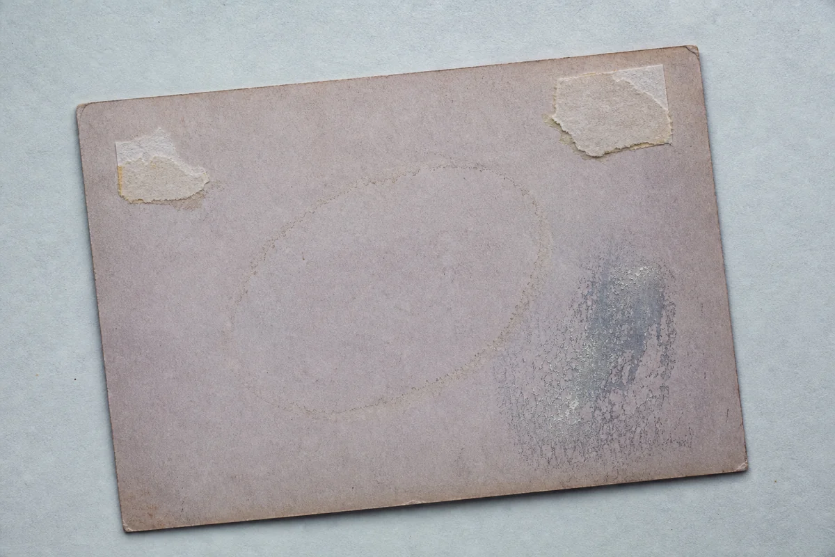Reverse of an old photograph with torn hinges, a tide mark, and silvering